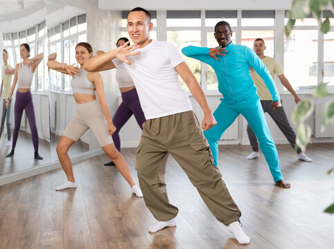 Emotional sporty young Asian dancer rehearsing modern krump dance moves during group workout in studio