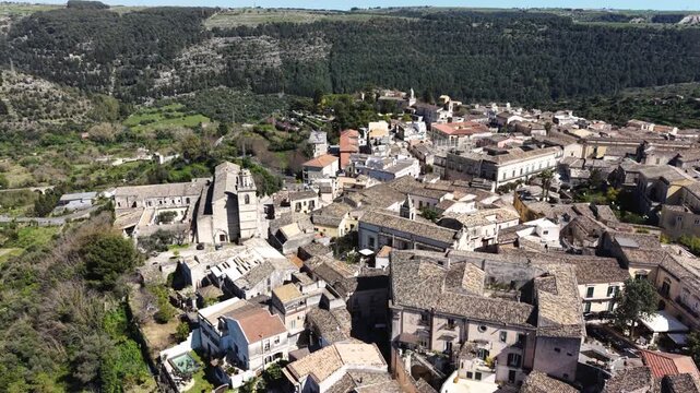 Aerial view of the historic stone buildings and church of Ragusa Ibla nestled among lush green hills and valleys in Ragusa, Sicily, Italy.