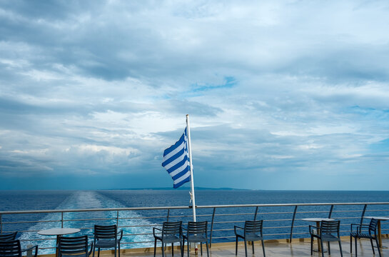 Boat terrace with Greek flag waving over sea and cloudy sky