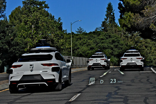 Heads-up speed display projected on front windshield following three Waymo cars accelerating past 23 mph to speed limit of 35 mph.