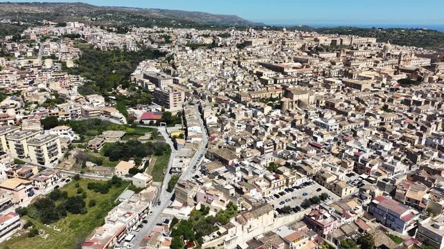 Aerial view of the historic Baroque architecture and limestone buildings of Noto surrounded by rolling hills and green landscape in Noto, Sicily, Italy.