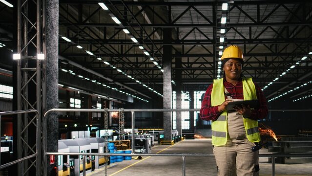 African American female personnel inspecting heavy machinery and framework components on a tablet, modern engineering plant, Metalwork environment defined by large-scale production line.