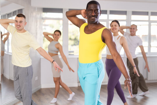 Enthusiastic adult african american man in colorful attire dancing expressive salsa during group class in mirrored choreography studio