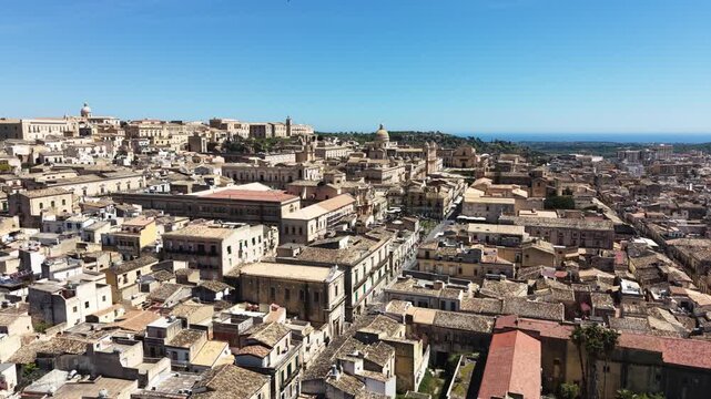 Aerial view of the historic baroque architecture and limestone buildings of the old town under a clear blue sky in Noto, Sicily, Italy.