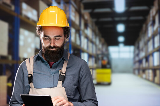 Warehouse worker verifying list of stock packages stored on racks, looking at storage labels and order numbers on pallets. Packaging engineer managing shipment and delivery, inventory management.