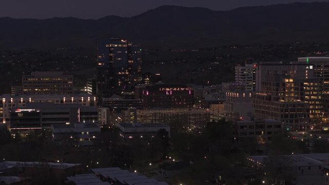 Atmospheric nighttime slow panning drone shot of downtown Boise skyline from the river, Idaho. City lights sparkle with traffic on 13th & 11th streets and the iconic Arthur Building visible.