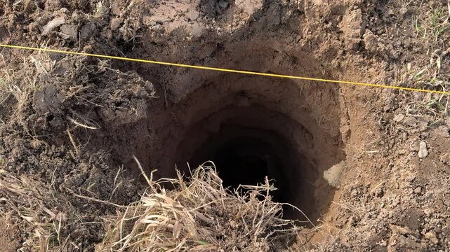 Deep round holes for fence posts, surveyor marking layout with yellow string, landscaper clearing loose soil, contractor preparing
