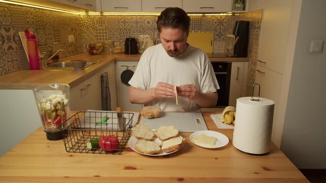Man placing yellow cheese slices on bread rolls in kitchen morning