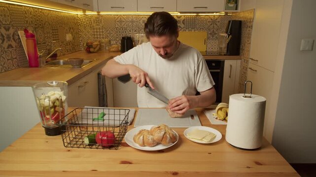 Man slicing bread rolls on cutting board in rustic kitchen morning