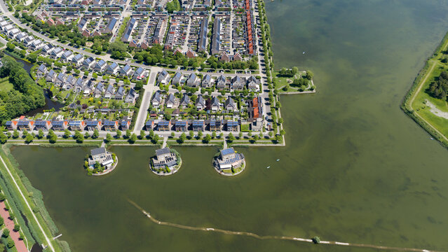 Aerial view of modern residential houses with solar panels and unique circular island homes along the waterfront in Heerhugowaard, North Holland, Netherlands.