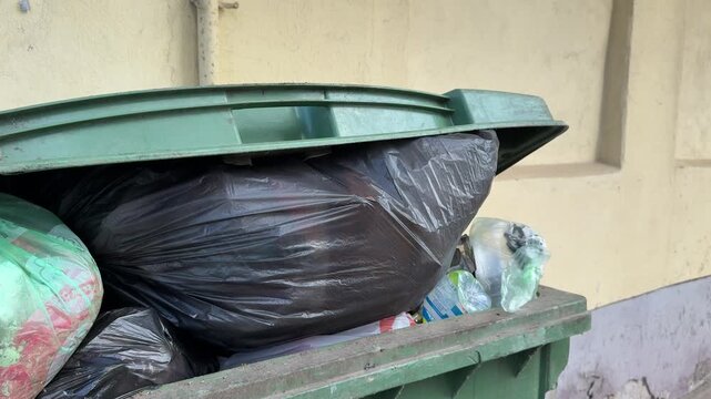 Close-up overflowing green dumpster loaded cardboard and construction debris including insulation, taped bags, crushed packaging