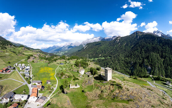 Aerial view of Chaste Steinsberg castle ruins on a rocky hill overlooking the village houses and alpine mountains under a blue sky in Scuol, Graubunden, Switzerland.