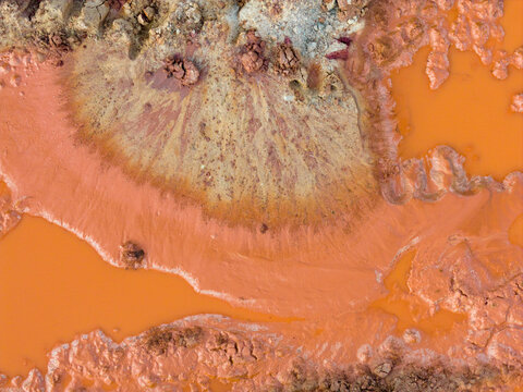 Aerial view of textured orange clay and muddy pools with fan-like sediment patterns at an industrial excavation site in Coimbra, Coimbra District, Portugal.