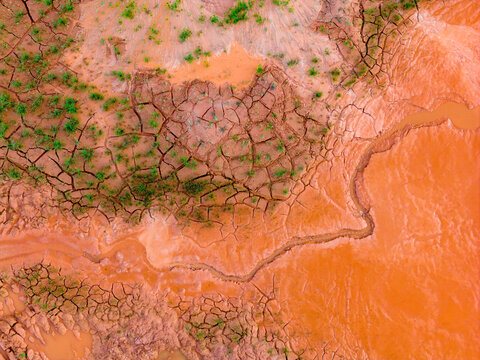 Aerial view of cracked red clay soil with sparse green vegetation and muddy orange water channels in Coimbra, Coimbra District, Portugal.