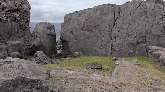 Q'enqo Archaeological Complex, Cusco, Peru - 20 June 2024. Large carved limestone formations and a ceremonial passage at the Inca sanctuary, with footpaths crossing the rocky ground under cloudy skies