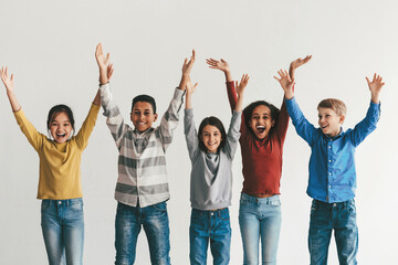 Obraz premium Joyful Diverse Children Including Boys And Girls Of Various Ethnicities, Smiling And Celebrating Together With Hands Raised, Standing In A Bright Studio, Youthful Energy And Togetherness Concept