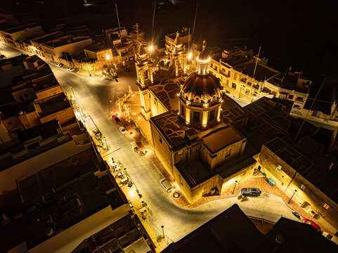 Aerial view of the illuminated Sannat Parish Church with its prominent dome and bell towers at night in Sannat, Gozo Region, Malta.