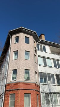 White brick apartment against blue sky. Sunlit multistorey facade with rows of windows, balconies and chimney framed by bare