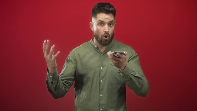 Man holding smartphone, gesturing with hand and speaking into phone in red studio; frustration communication.