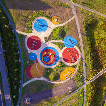Aerial view of the colorful circular play areas and walking paths at Maybury Drive playground surrounded by green landscape in Edinburgh, Scotland, United Kingdom.