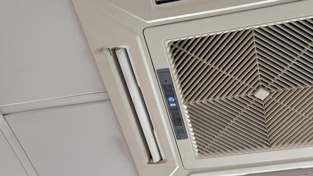 Ceiling cassette air conditioner unit mounted in suspended office ceiling grid, white grille and vents, closeup inspection