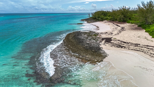 Aerial view of Preacher's Cave Beach with turquoise waters, white sand, and rocky shoreline in The Bluff Settlement, North Eleuthera, The Bahamas.