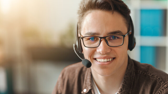 Smiling Young Caucasian Male Customer Service Agent Wearing Headset, Providing Support And Assistance While Sitting At Office Desk, Working With Clients, Business Concept