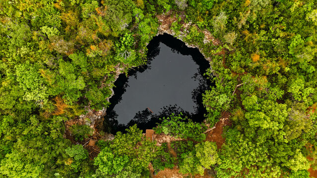 Aerial view of Sapphire Blue Hole surrounded by dense tropical forest and lush green vegetation in The Bluff Settlement, North Eleuthera, The Bahamas.