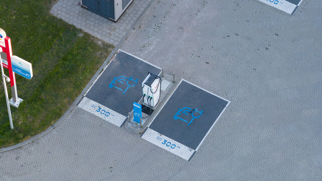Roosendaal, Netherlands - 25 April 2026: Aerial view of an electric vehicle charging station with blue icons on paved parking spots and a white charging unit.