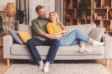 Obraz premium Smiling Senior Caucasian Sitting Together On Couch In Cozy Living Room, Embracing And Sharing Joyful Moments, Enjoying Each Other's Company, Home Environment, Lifestyle Concept