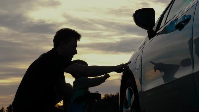 Baby and loving parent connect charging cable into an electric car. Touching moment of family bonding, exploring EV charging at sunset, sustainable energy, green technology