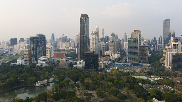 Bangkok, Thailand - 05 February 2026: Aerial view of the city skyline featuring modern skyscrapers overlooking the lush greenery and lake of Lumphini Park under a hazy sky.