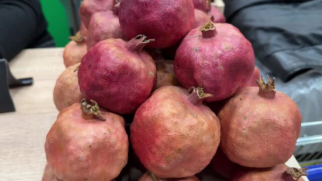 Red Azerbaijani mountain pomegranates stacked on juice shop counter, symmetrical pyramid of ripe crimson fruits in wooden crate