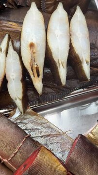 Cold smoked halibut steaks on counter, close-up of glistening white flesh and brown skin on chilled tray, market display suggests