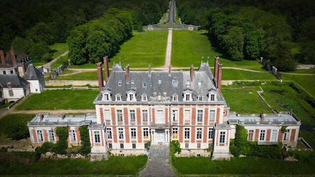 Savigny-le-Temple, France - 28 May 2023: Aerial view of the historic Chateau de la Grange featuring its brick facade and slate roof, surrounded by expansive green lawns and lush forest.