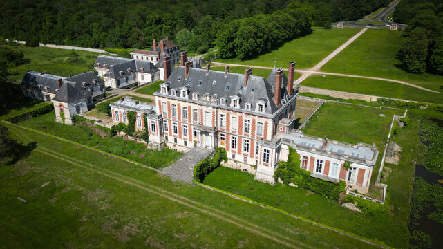 Savigny-le-Temple, France - 28 May 2023: Aerial view of the historic Chateau de la Grange featuring its red brick facade and slate roofs surrounded by lush green lawns and dense forest.