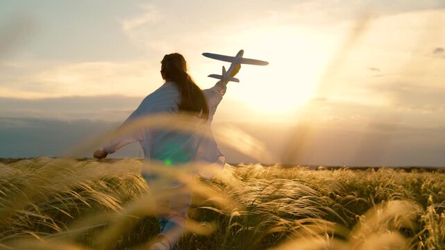 Happy kid girl runs with toy airplane on field in sunset light. Child play toy airplane. Kid aviator dreams of flying becoming pilot. Little girl child wants to become pilot astronaut sky. Slow motion
