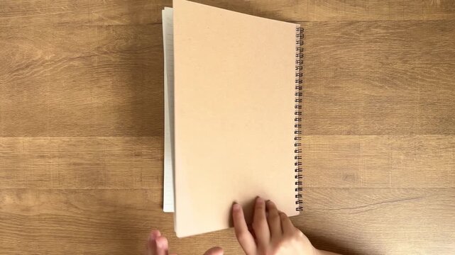 Child Hands Opening a Large Notebook as an Adult Hand Gently Adjusts Its Position on a Wooden Table, 4K Silent Video