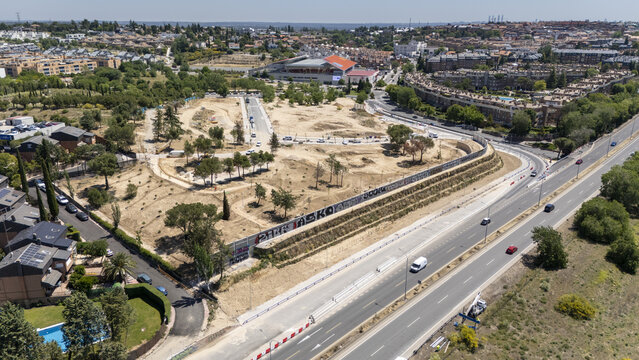 Las Rozas de Madrid, Spain - 31 May 2026: Aerial view of a large open field with scattered trees and dirt paths adjacent to a multi-lane road and residential neighborhoods.