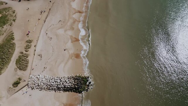 Top-down drone view of Hengistbury Head shoreline, Bournemouth, Dorset, UK. Coastline with sea, rocks and beach.
