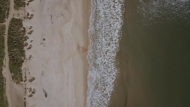 Top-down drone view of Hengistbury Head shoreline, Bournemouth, Dorset, UK. Waves lapping on coastline with sea, rocks and beach.