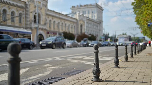 Urban city street scene with blurred car traffic and metal sidewalk bollards on a sunny day.