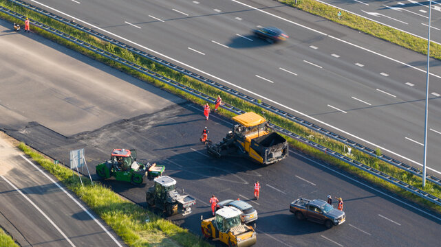 Nieuwegein, Netherlands - 09 May 2026: Aerial view of road construction workers and heavy machinery paving asphalt on a highway under bright sunlight.