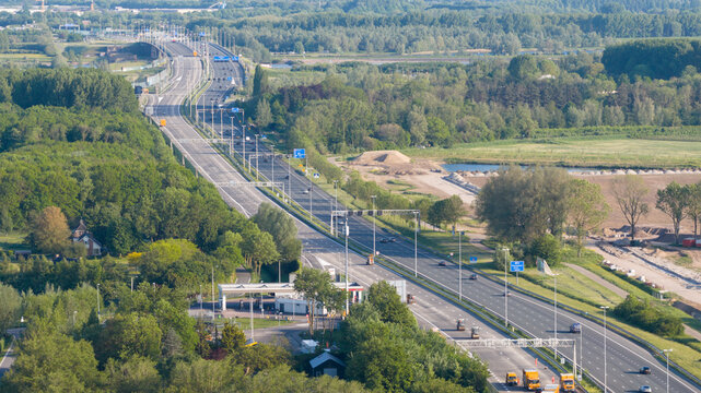 Nieuwegein, Netherlands - 09 May 2026: Aerial view of the A2 motorway with traffic flowing past a service station and dense green forests under bright daylight.