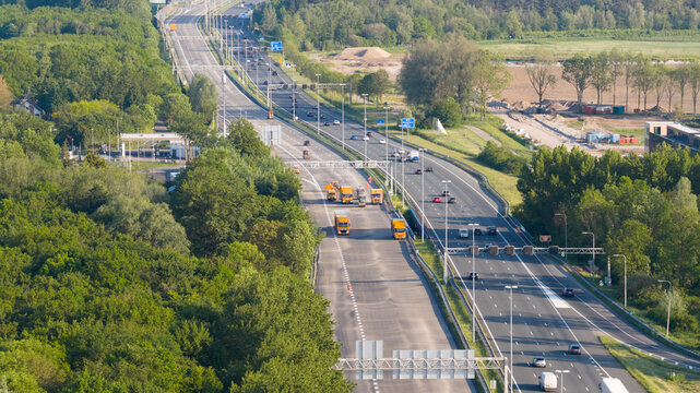 Nieuwegein, Netherlands - 09 May 2026: Aerial view of a busy highway with road maintenance vehicles and traffic surrounded by dense green forests and fields.