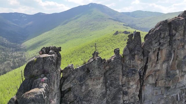 Drone overview of the shadow side of an ancient natural mountain formation with a rock climber hanging on the wall and a dead tree in the foreground against wild spring taiga nature