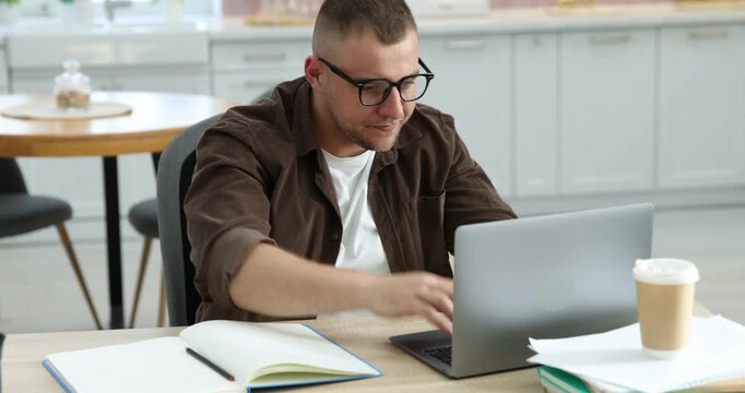 Workaholic. Man in glasses working with laptop at wooden desk in kitchen, camera moving forward