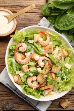 Tasty Caesar salad with shrimps on wooden table, flat lay
