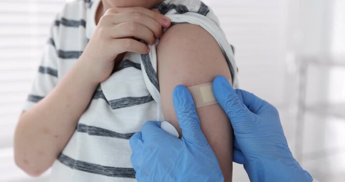 Nurse in medical gloves applying adhesive bandage onto patient's arm after vaccination indoors, closeup. Camera moving in and out