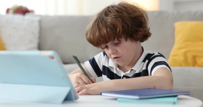 Tired boy with tablet doing homework at table in room